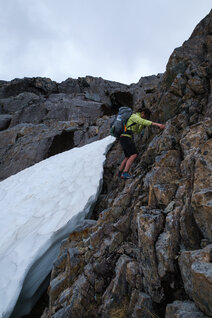 Hiker climbing in the rocks beside a snow field
