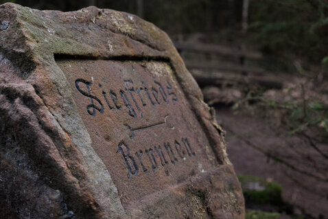Ein behauener Sandsteinblock mit der Inschrift 'Siegfriedsbrunnen'