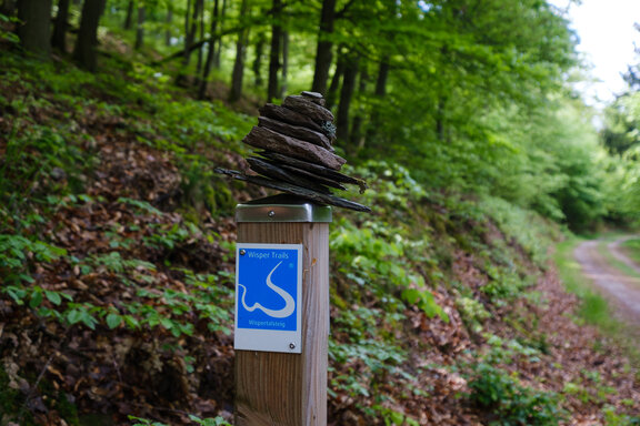 Wanderweg Zeichen des Wispertalsteigs im Taunus, montiert an einem Pfosten auf dem ein kleines Steinmännchen sitzt