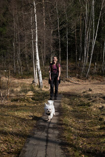 Eine junge Frau und ein Hund laufen über einem Bohlensteg über ein Moor
