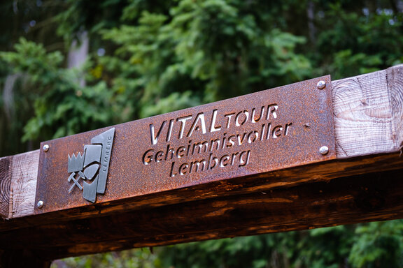 Wanderportal - Hölzerner Torbogen mit einer Metallplakette mit Aufschrift 'VitalTour Geheimnisvoller Lemberg'