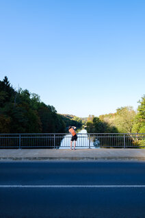 Eine Frau mit einem orangenen Rucksack steht auf der Salinenbrücke in Bad Kreuznach und fotografiert den Fluss Nahe