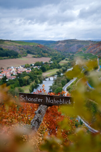 Wooden sign with inscription 'Schönster Naheblick' in the background a view into the Nahe Valley