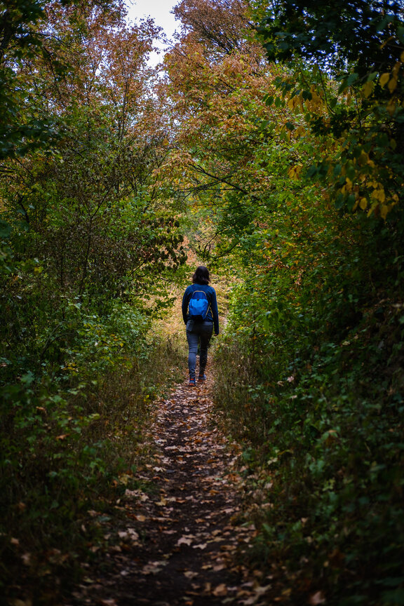 Woman walking through narrow footpath with leaves through the woods in the Nahetal valley
